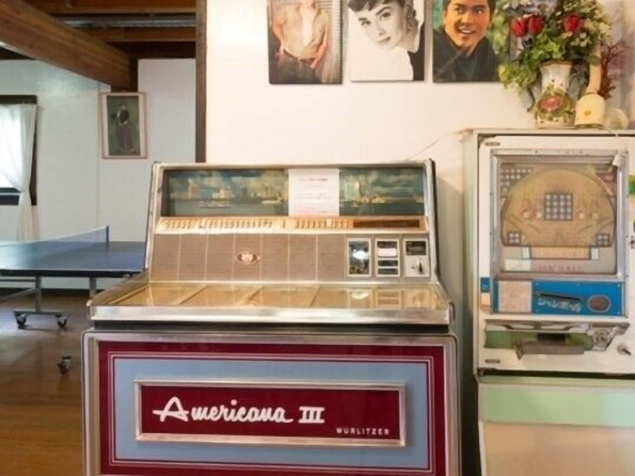 A vintage jukebox and a table tennis table in a room with framed pictures on the wall.