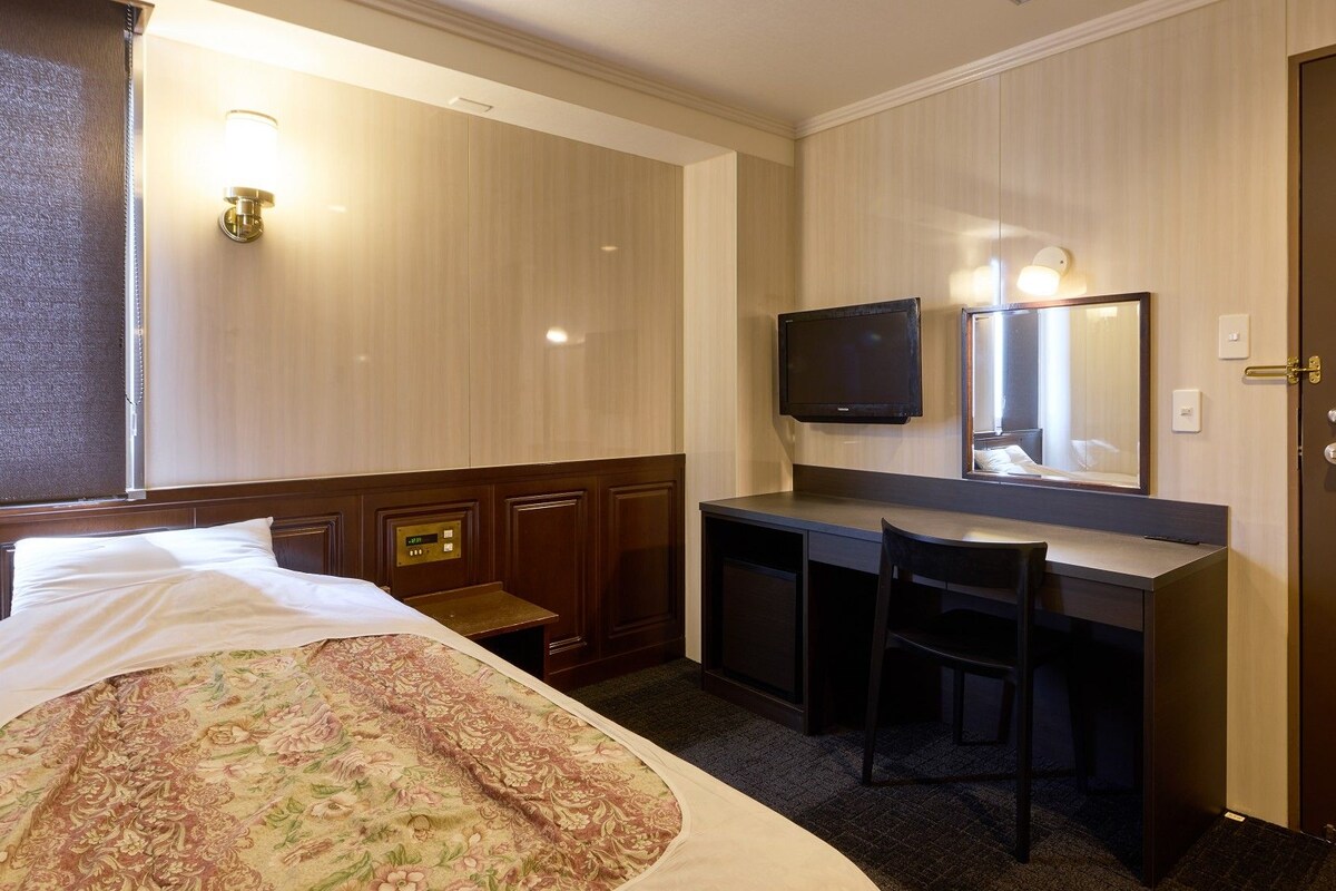A hotel room with a bed, desk, chair, television, and a door.