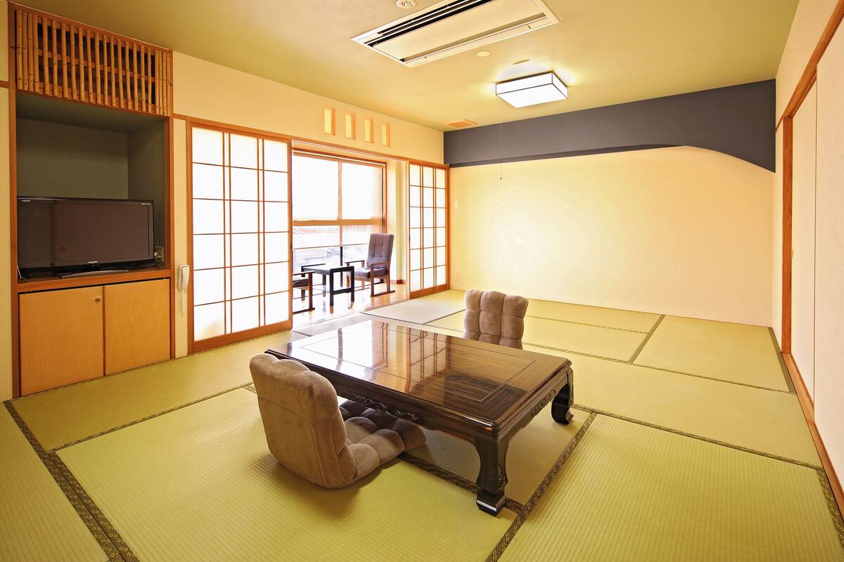 Una habitación tradicional japonesa con suelo de tatami, una mesa baja y un televisor sobre un mueble.