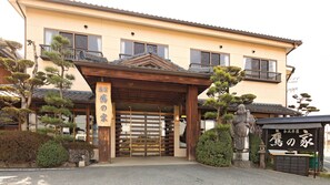 A traditional Japanese building with a wooden entrance gate, a stone statue, and well-maintained landscaping. - Ueki Onsen Takanoya (Kumamoto)