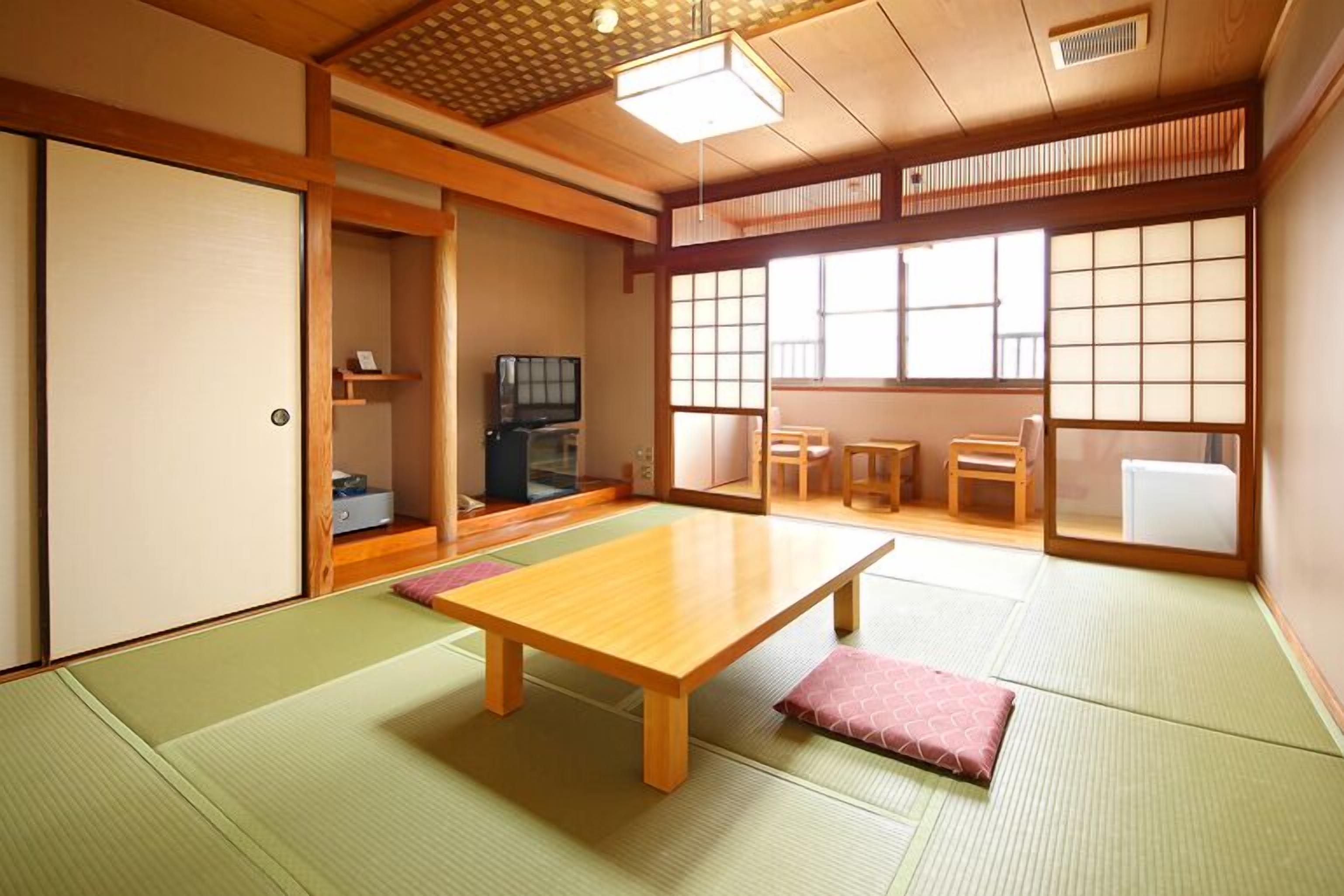 Una habitación japonesa tradicional con suelo de tatami, una mesa de madera baja, puertas correderas y un televisor.