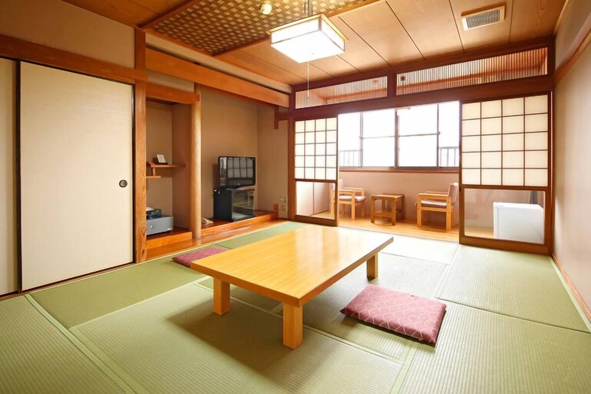 Una habitación japonesa tradicional con suelo de tatami, una mesa de madera baja, puertas correderas y un televisor.
