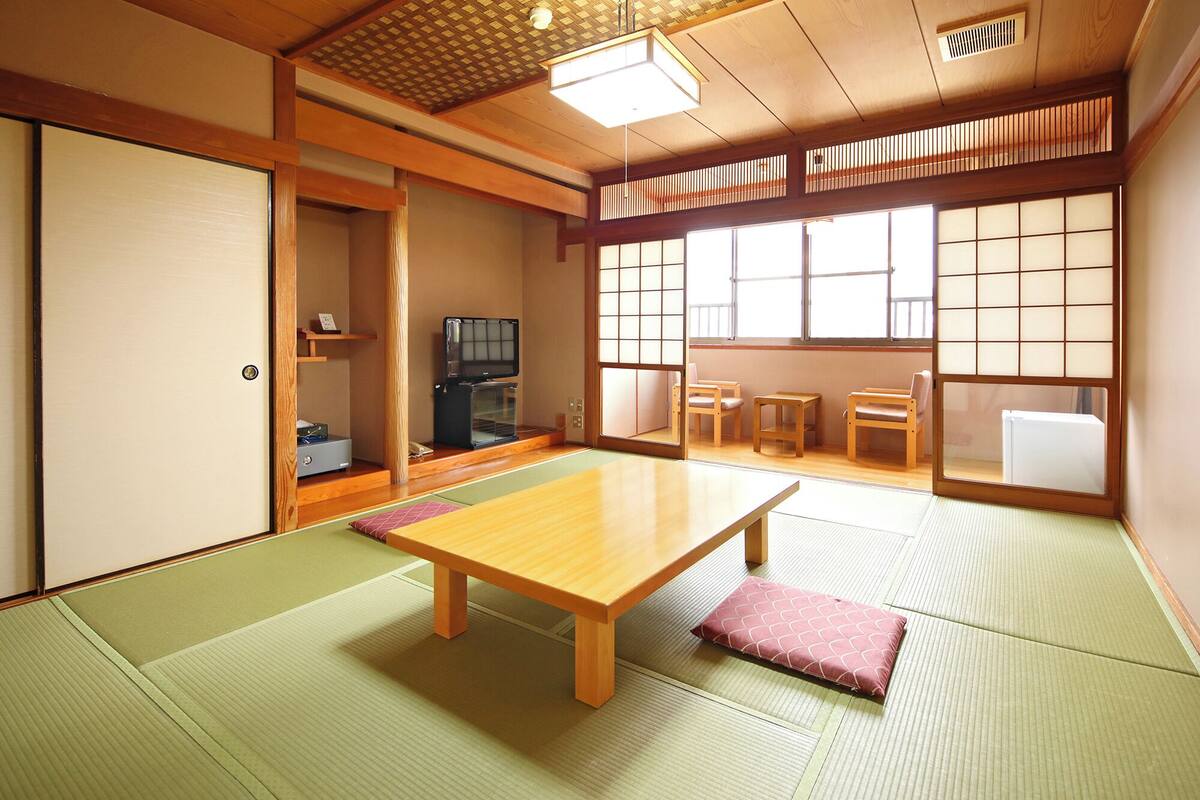 Una habitación japonesa tradicional con suelo de tatami, una mesa baja, un televisor y puertas correderas.