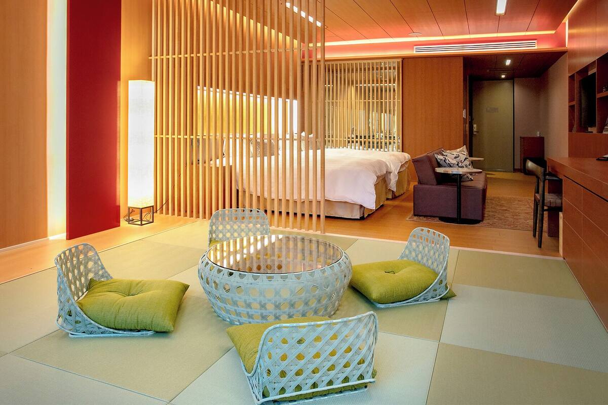 A hotel room with a bed, a sitting area with chairs, a small table, and a desk with a computer.