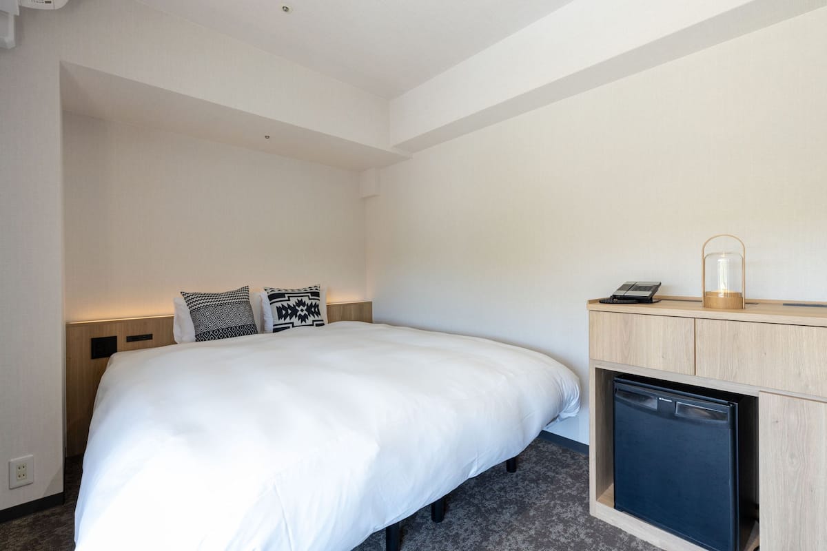 A hotel room with a bed, bedside table, lamp, and a built-in mini fridge.