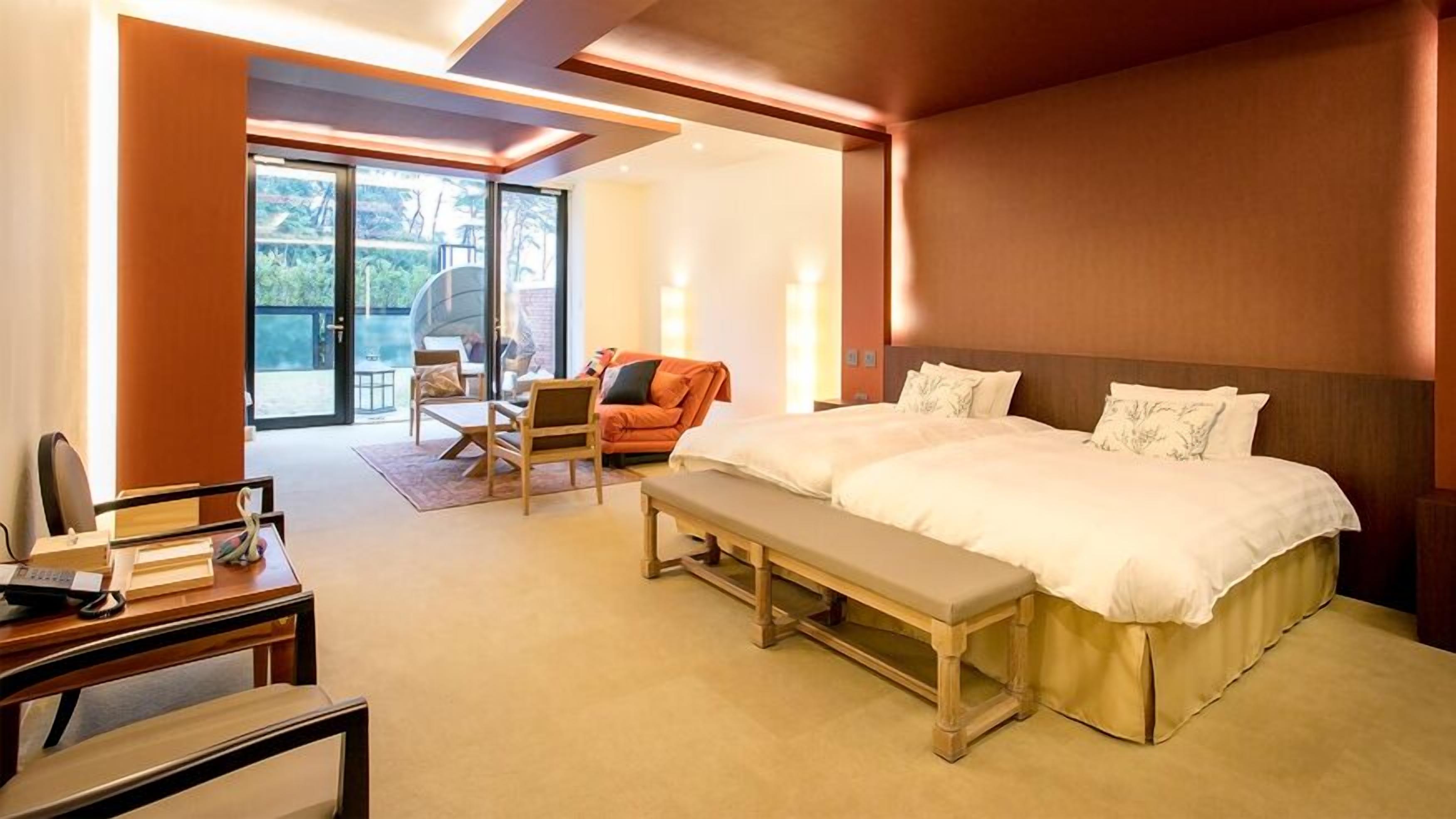 A hotel room with a large bed, a desk, a chair, and a view through a glass door.