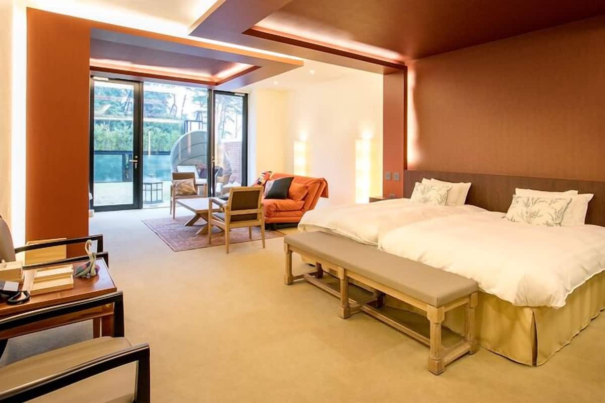A hotel room with a large bed, a desk, a chair, and a view through a glass door.