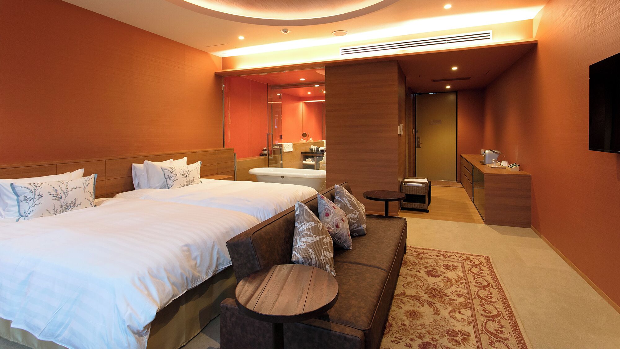 A hotel room with a large bed, a sofa, a small table, a bathroom, and a TV.