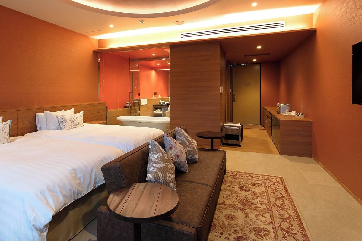 A hotel room with a large bed, a sofa, a small table, a bathroom, and a TV.