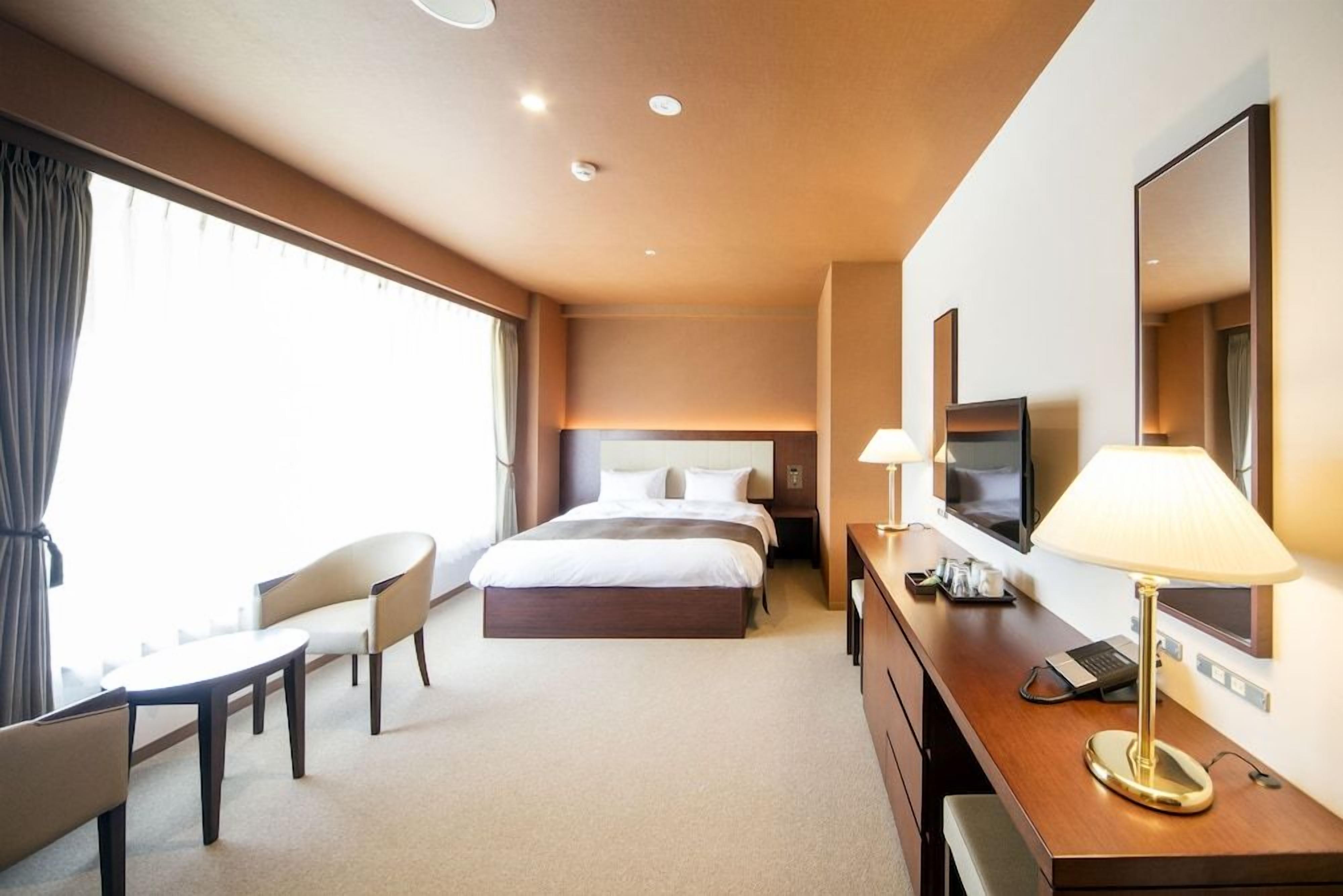 A hotel room with a bed, a desk, a chair, a TV, and a lamp.