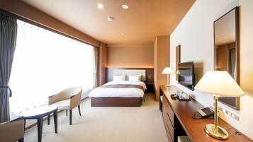 A hotel room with a bed, a desk, a chair, a TV, and a lamp.