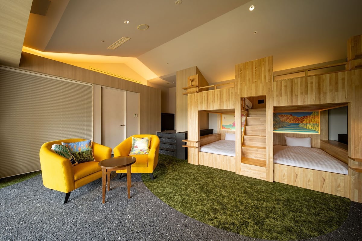 A modern room with a yellow sofa, a small table, and a bunk bed with a painting.