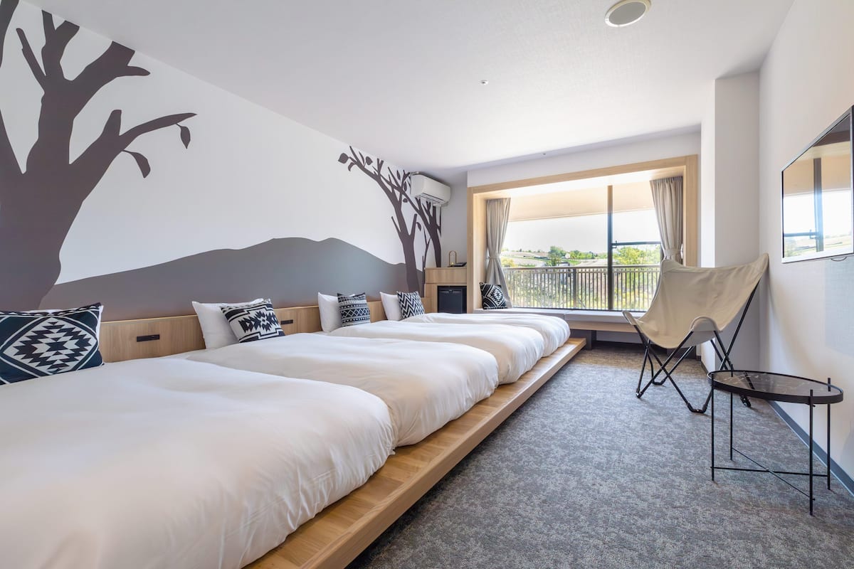 A hotel room with a large bed, a chair, a small table, and a balcony with a view.
