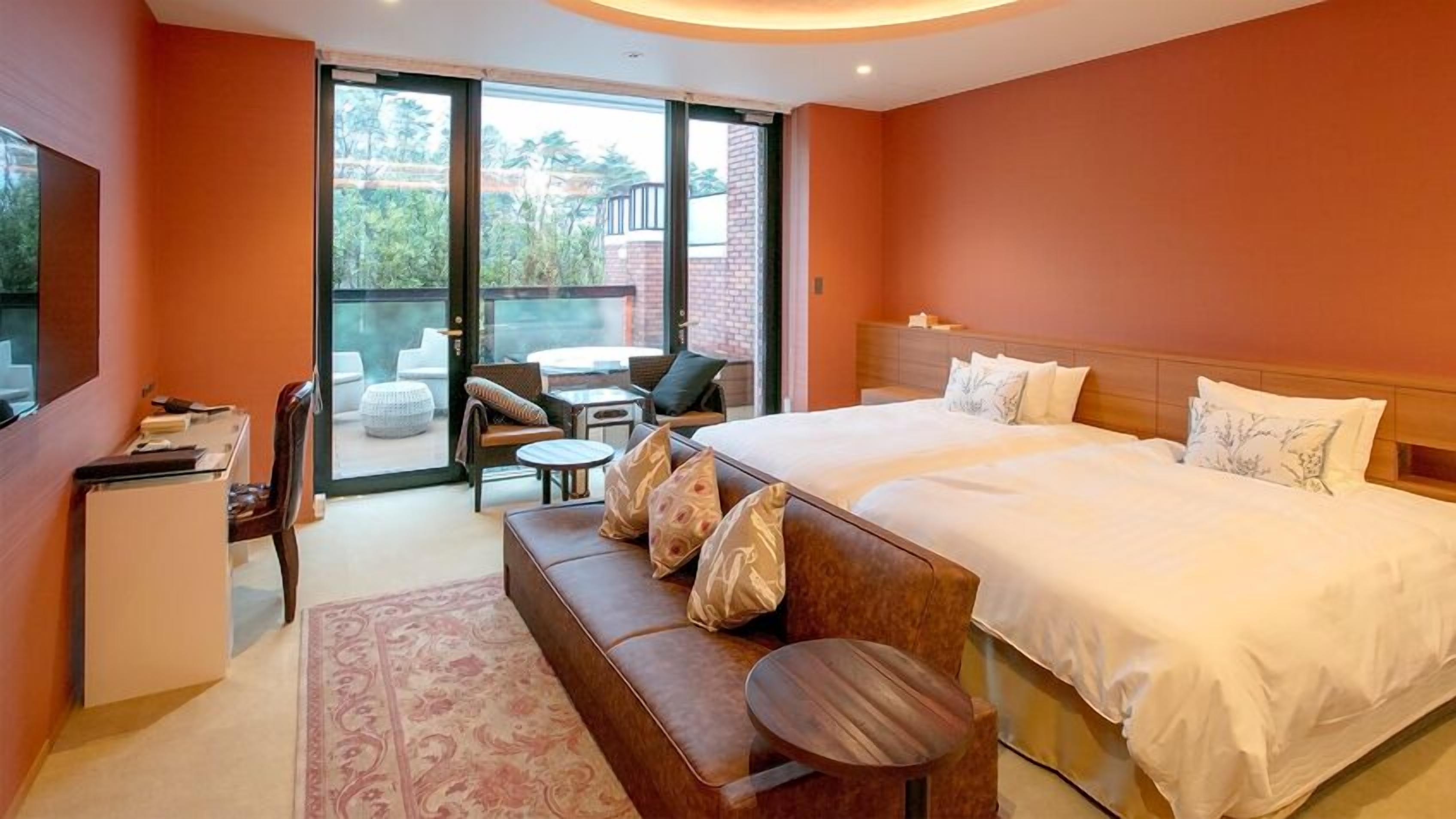 A hotel room with a large bed, a sofa, a desk, and a balcony with outdoor seating.