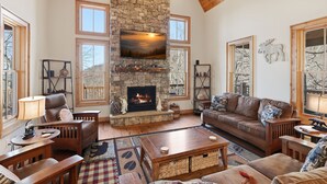 A cozy living room with a stone fireplace, wooden furniture, and large windows. - Birch and Squirrel - Quiet Luxury, Near Great Camp & Downtown Banner Elk (Banner Elk)