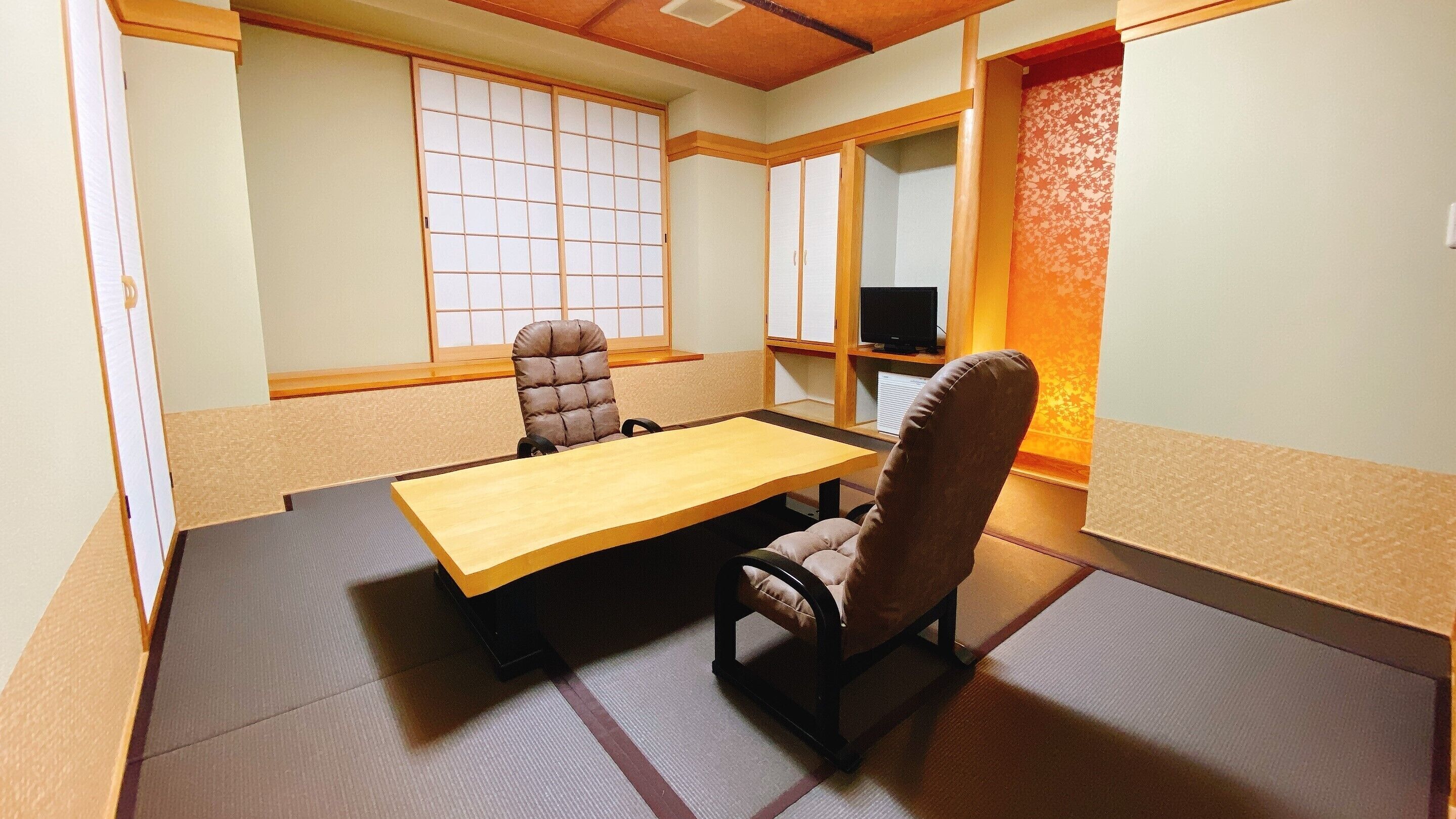 Una habitació japonesa tradicional amb tatami, una taula baixa, dues cadiretes amb coixins, un panell corredís shoji i una televisió.