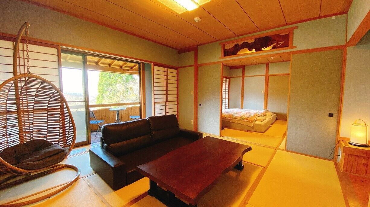Una habitació d'estil japonès tradicional amb sòl de tatami, sostre de fusta baix, un sofà, una cadira penjant i un llit amb futón.