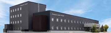 Un moderno edificio de hotel con techo plano, múltiples ventanas y una estructura vertical oscura destacada en la fachada.