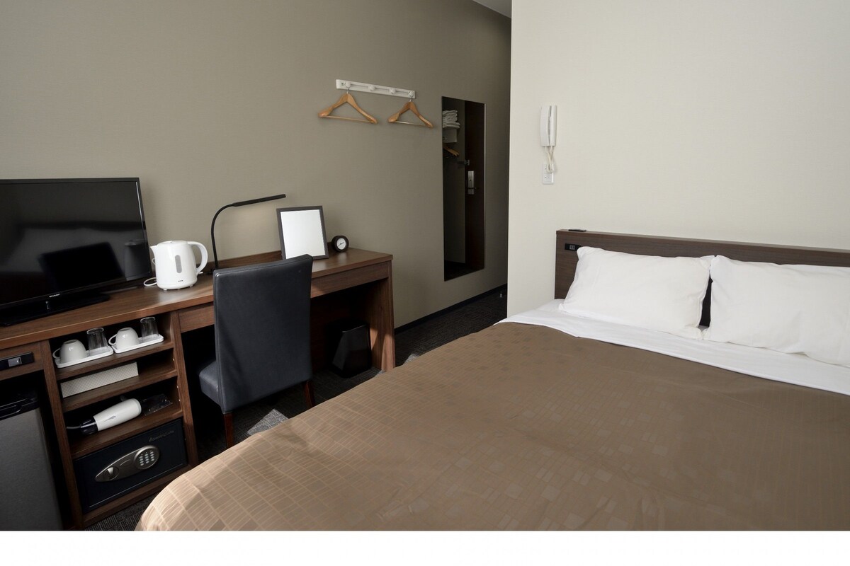 Habitación de hotel con cama, escritorio con televisor, cafetera, silla y armario.