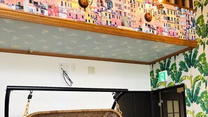 Uma cadeira de balanço de vime com almofadas, uma porta preta e uma parede com um mural colorido.