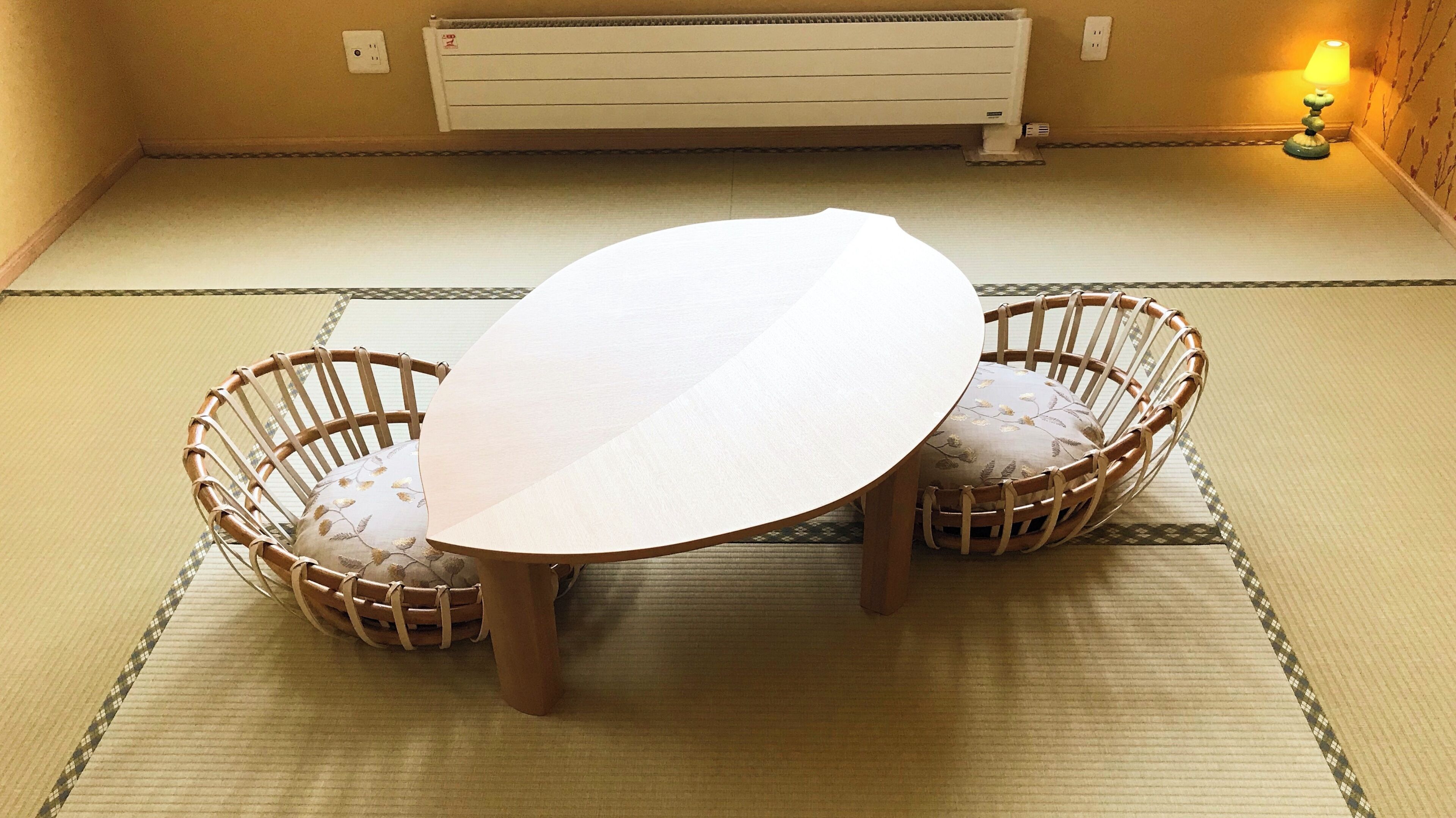 Una habitación con tatamis, una mesa baja y dos sillas tejidas.