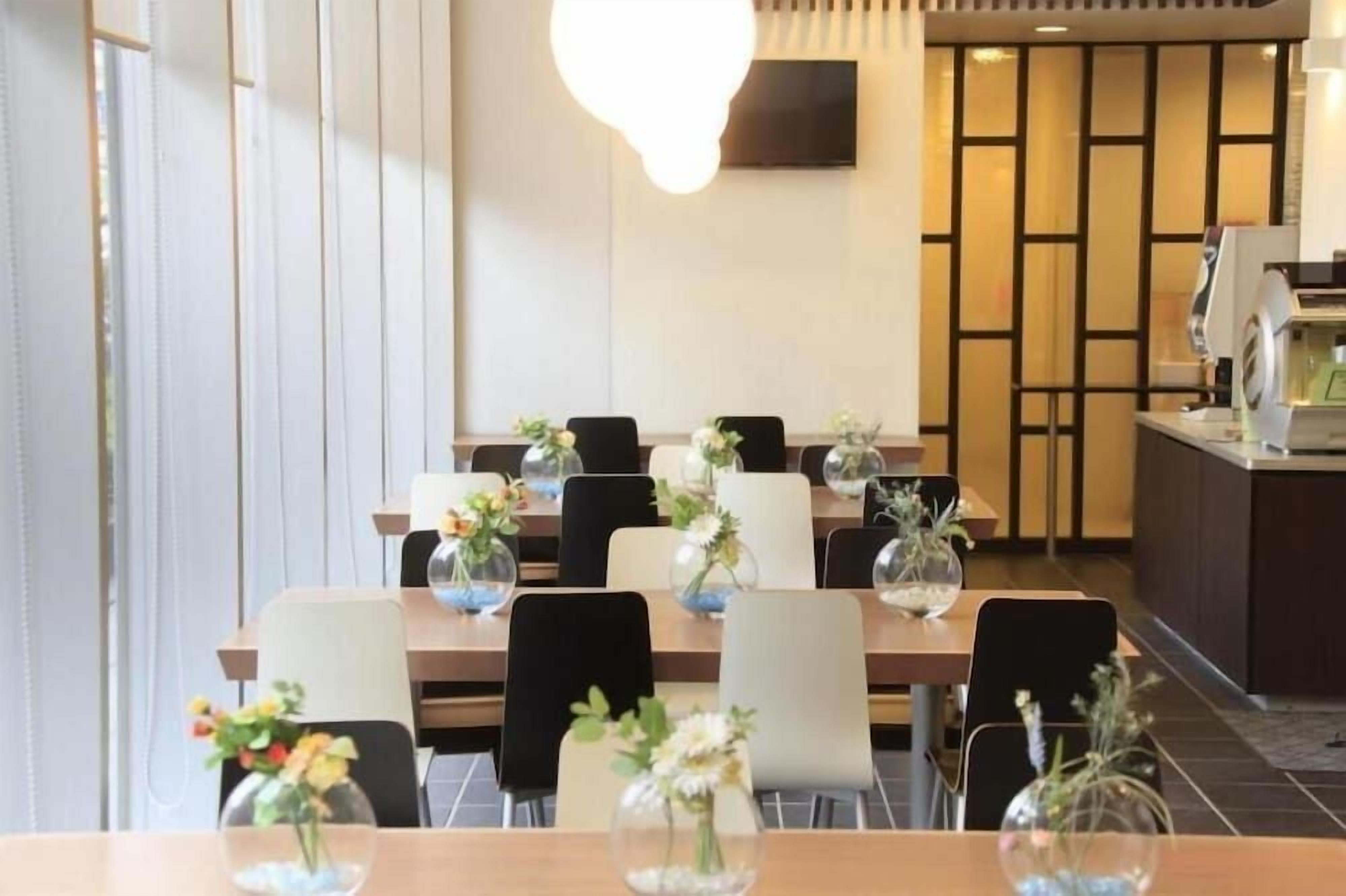 A hotel dining area with tables set for guests, each with a vase of flowers.