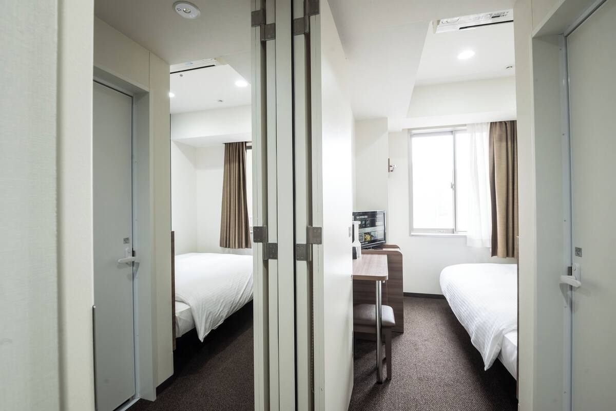 Una habitación de hotel con dos camas, un escritorio y un ventanal con cortinas.