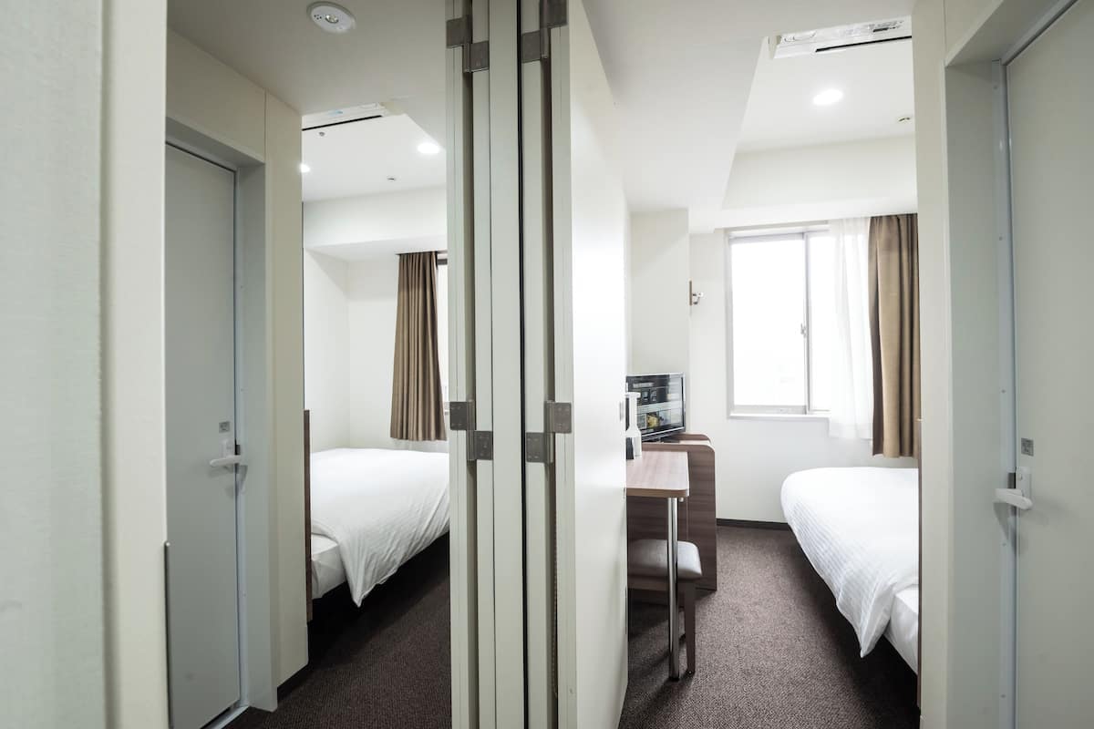 Quarto de hotel com duas camas, uma escrivaninha e uma janela com cortinas.