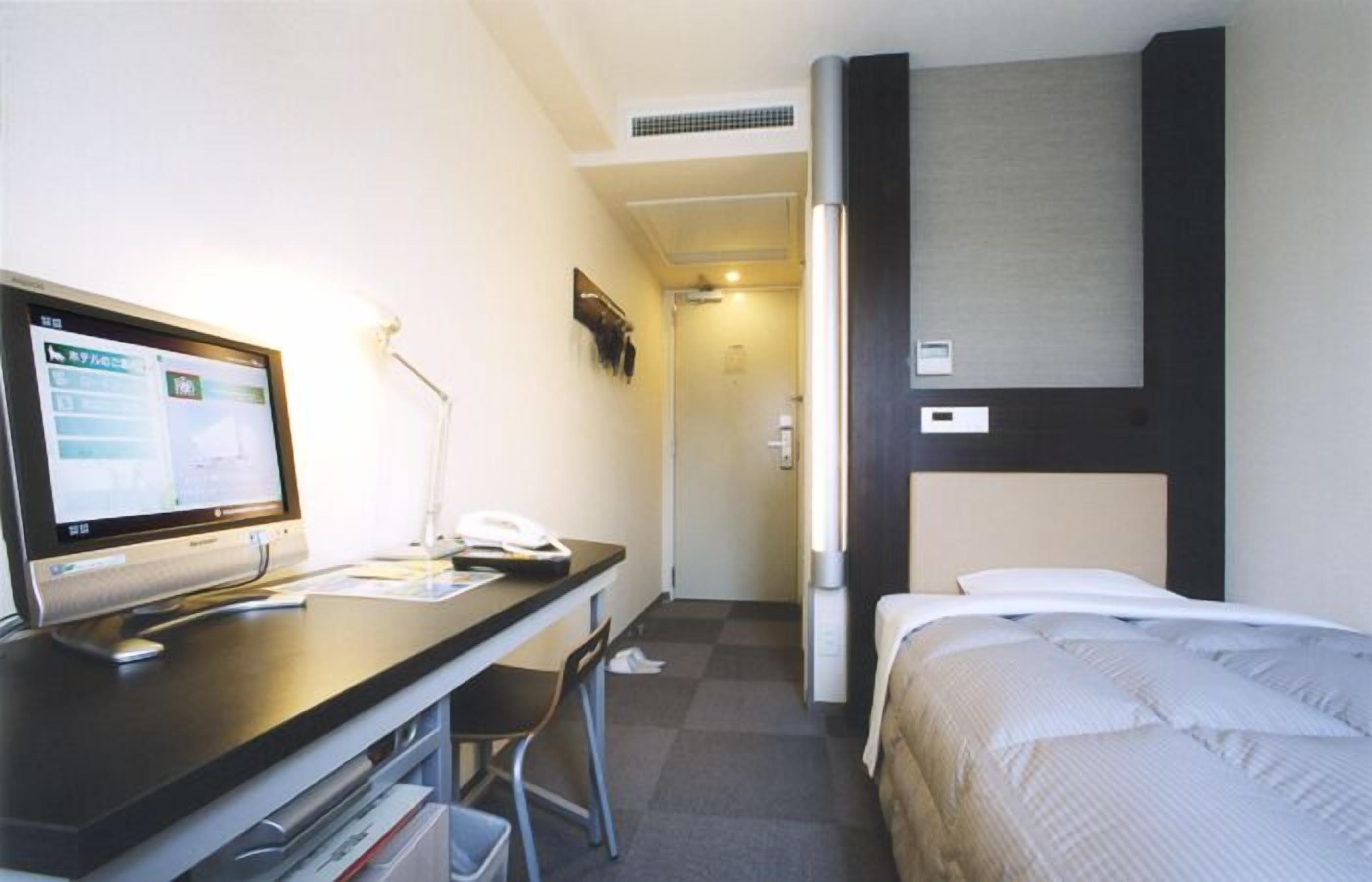 Ett hotellrum med ett skrivbord, en stol, en säng och en tv.