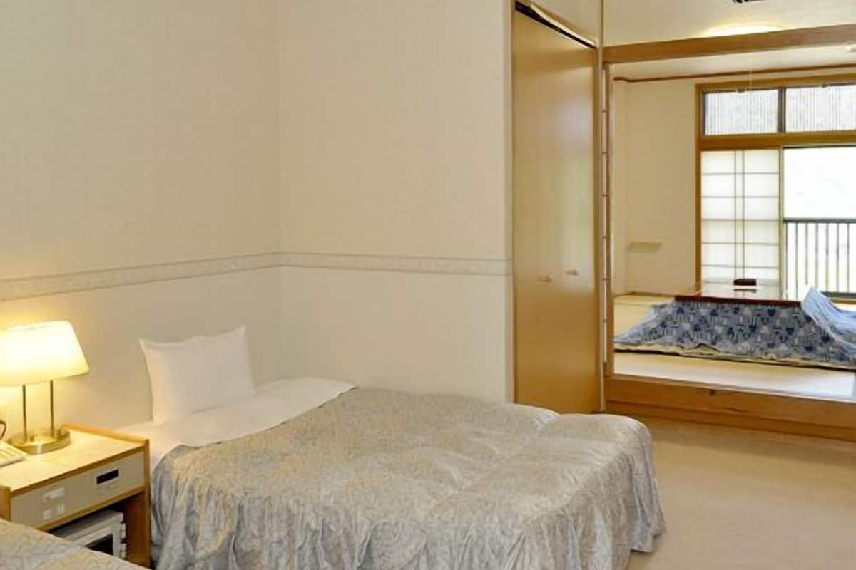 Ein Hotelzimmer mit zwei Betten, einem Nachttisch mit Lampe, einem Fenster mit Jalousien und einem Spiegel.