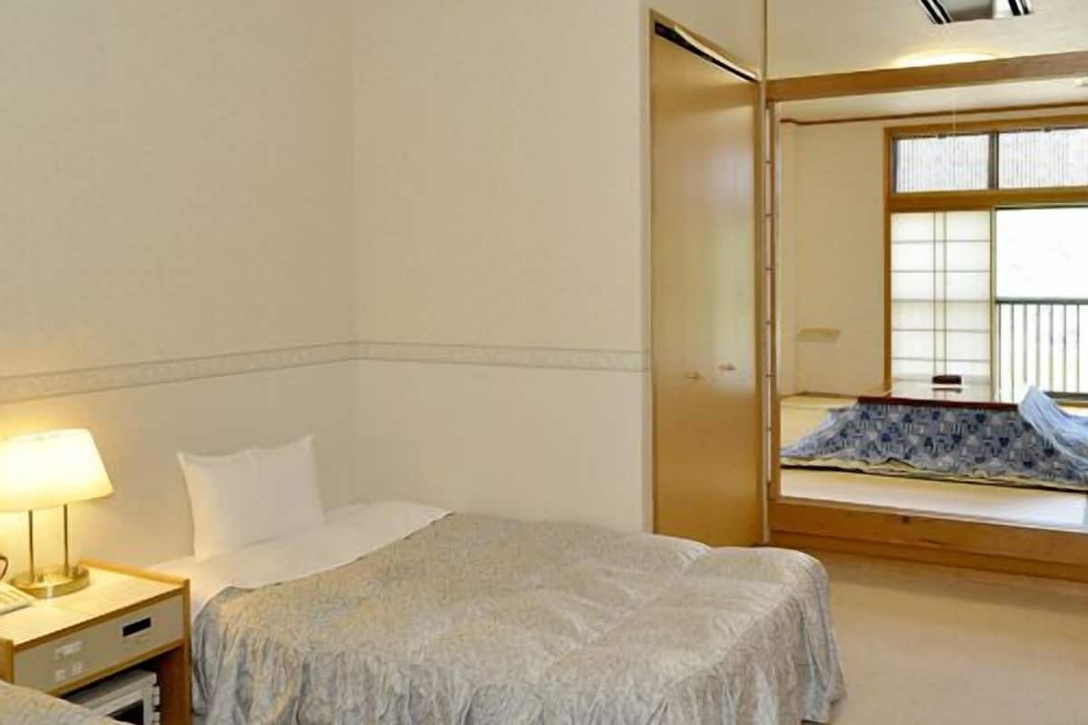 Ein Hotelzimmer mit zwei Betten, einem Nachttisch, einer Lampe und einem Fenster mit Jalousien.