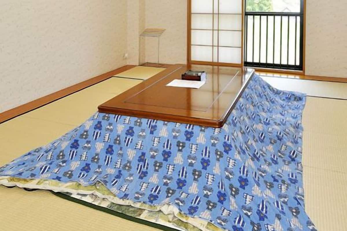 Ein Raum mit Tatami-Matten, einem niedrigen Tisch, einem Fenster mit Blick und einem gerahmten Bild an der Wand.