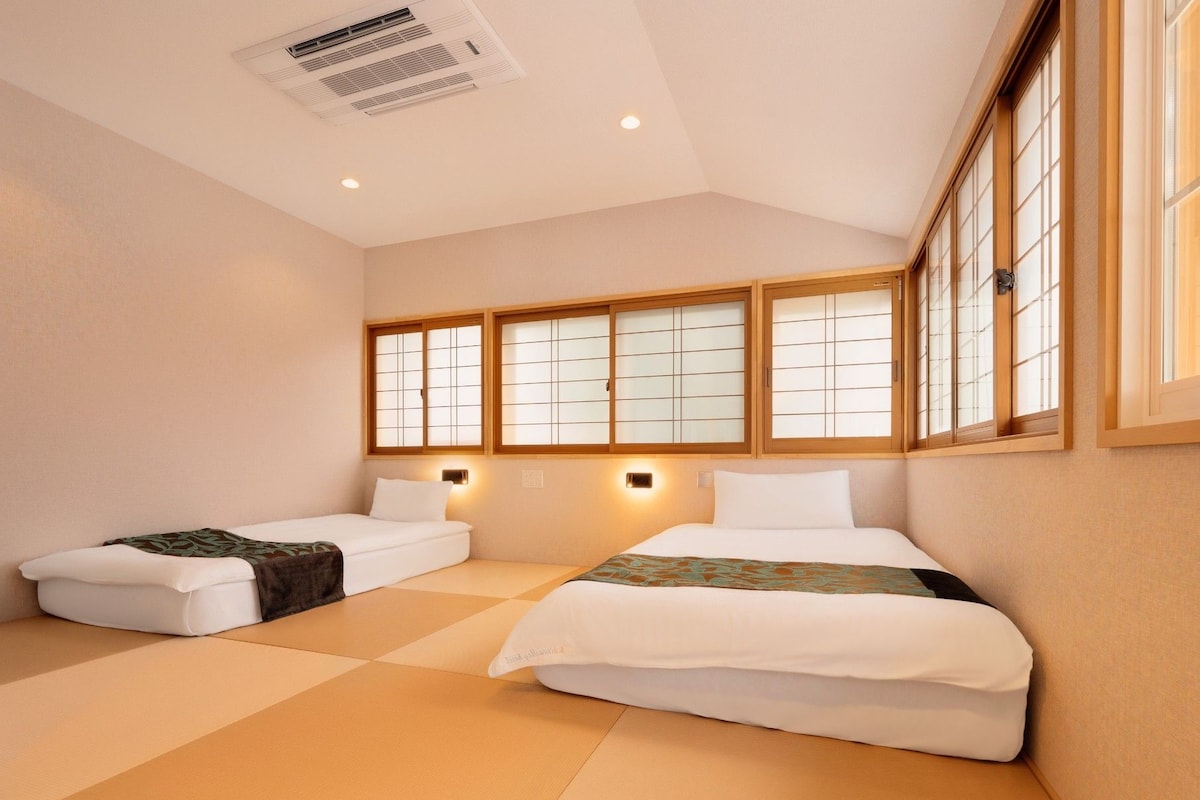 A hotel room with two beds, a large window with wooden frames, and a ceiling air vent.