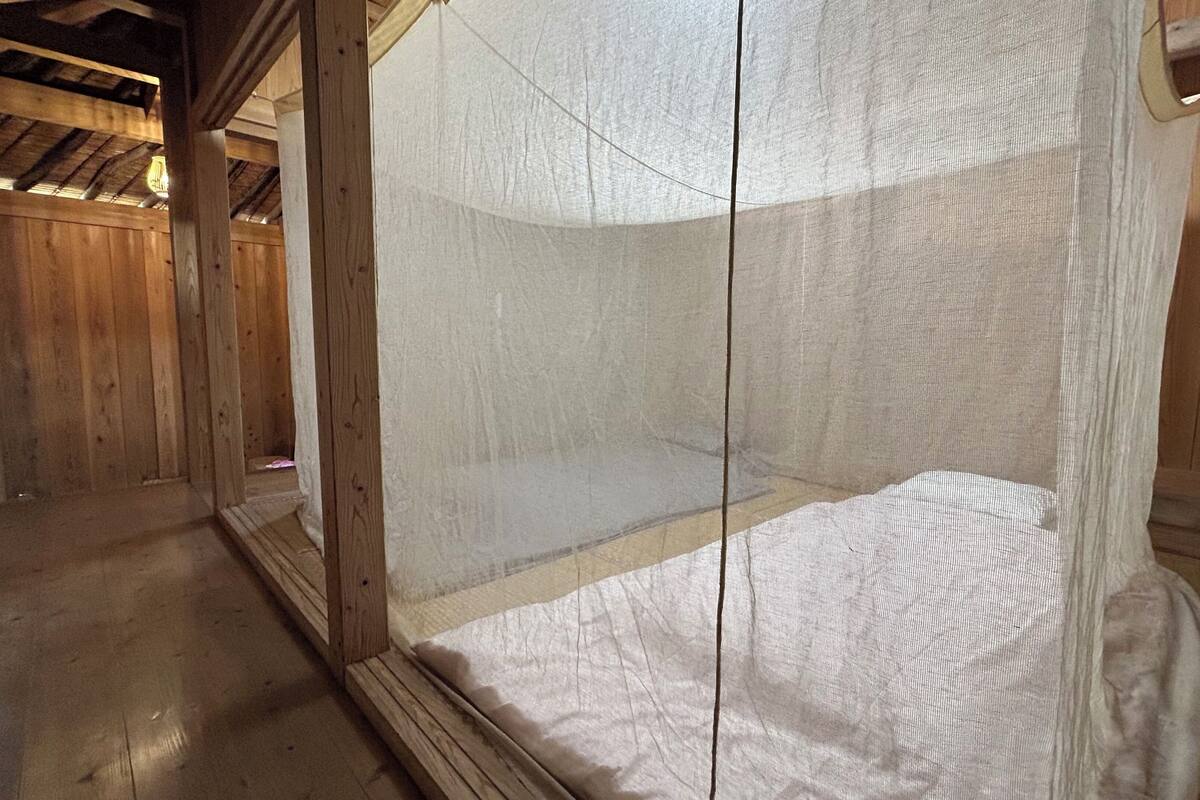 Quarto de madeira com uma cama e mosquiteiro.