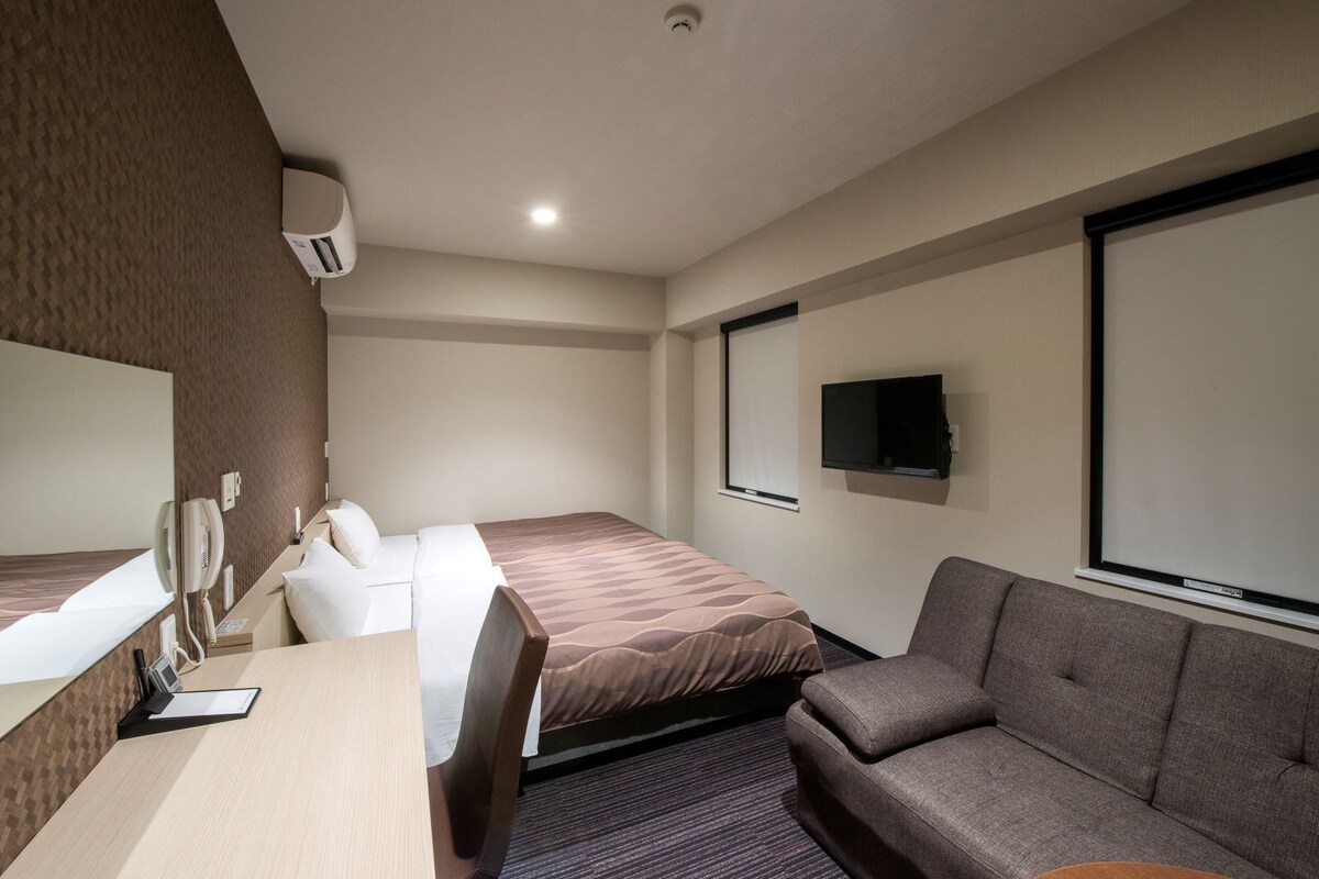 A hotel room with a bed, a desk with a telephone, a television, and a sofa.
