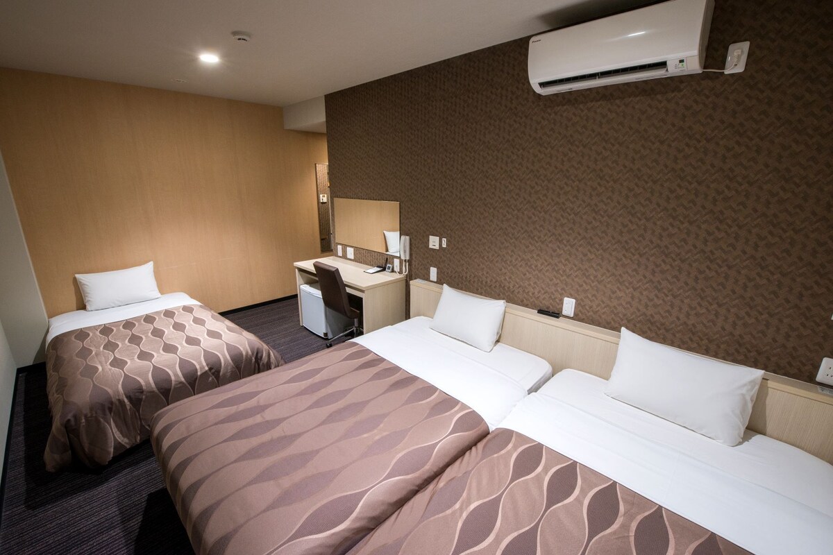 A hotel room with two beds, a desk, a chair, a mirror, and an air conditioning unit.
