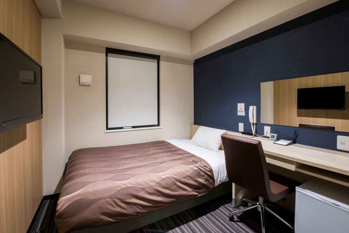 A hotel room with a bed, a desk, a chair, a television, and a mirror.