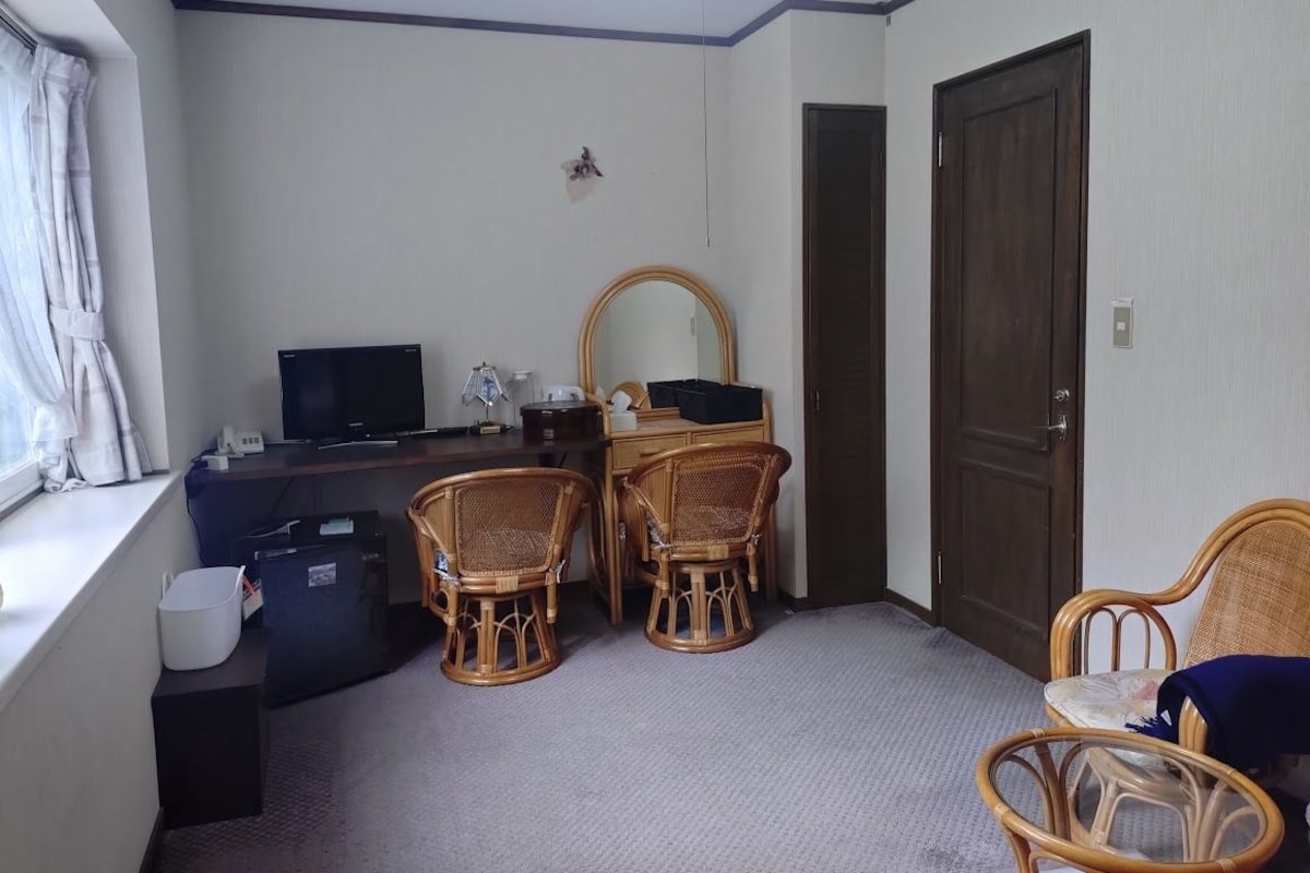 A room with a desk, two wicker chairs, a television, a mirror, and a door.
