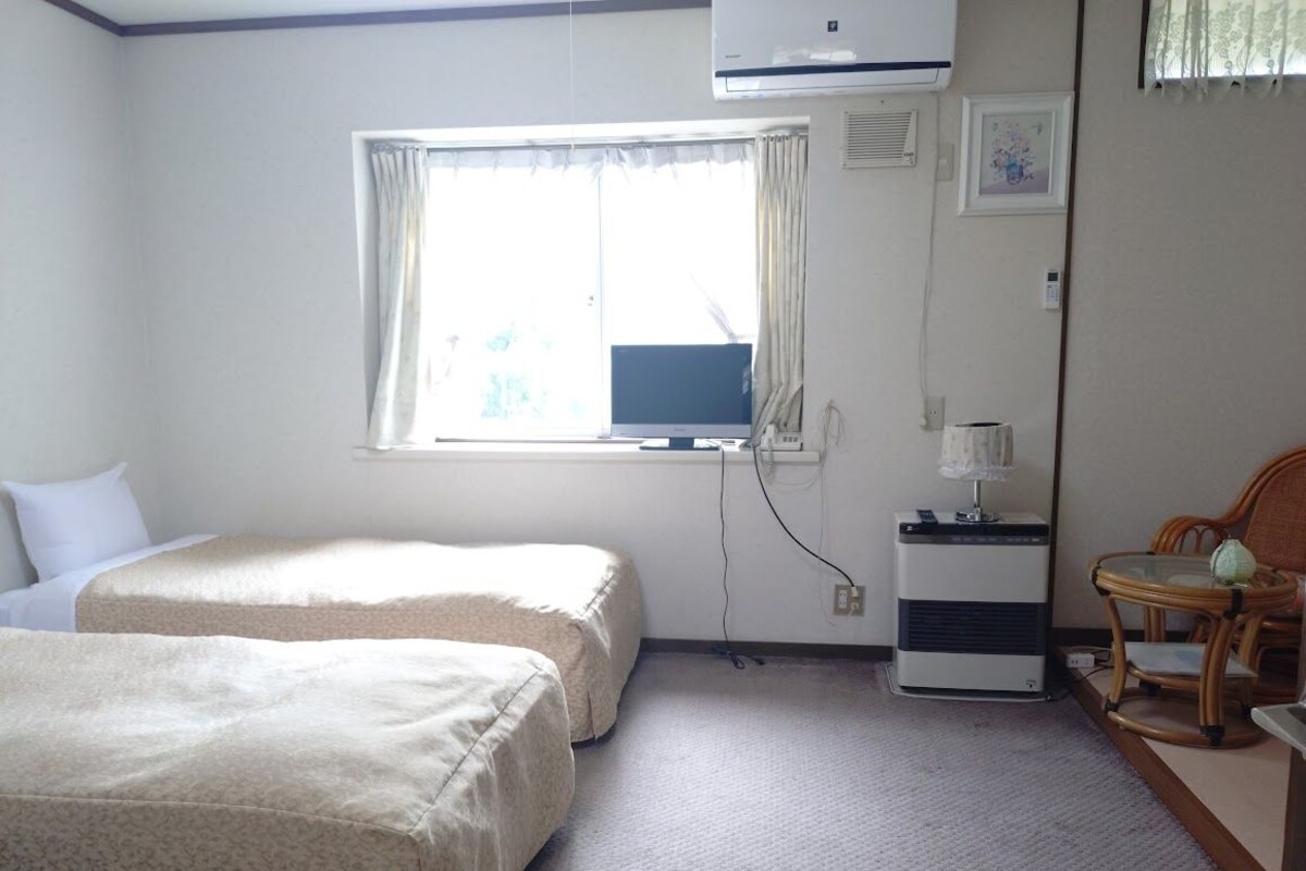 A hotel room with two beds, a desk with a computer, a chair, and a window with curtains.