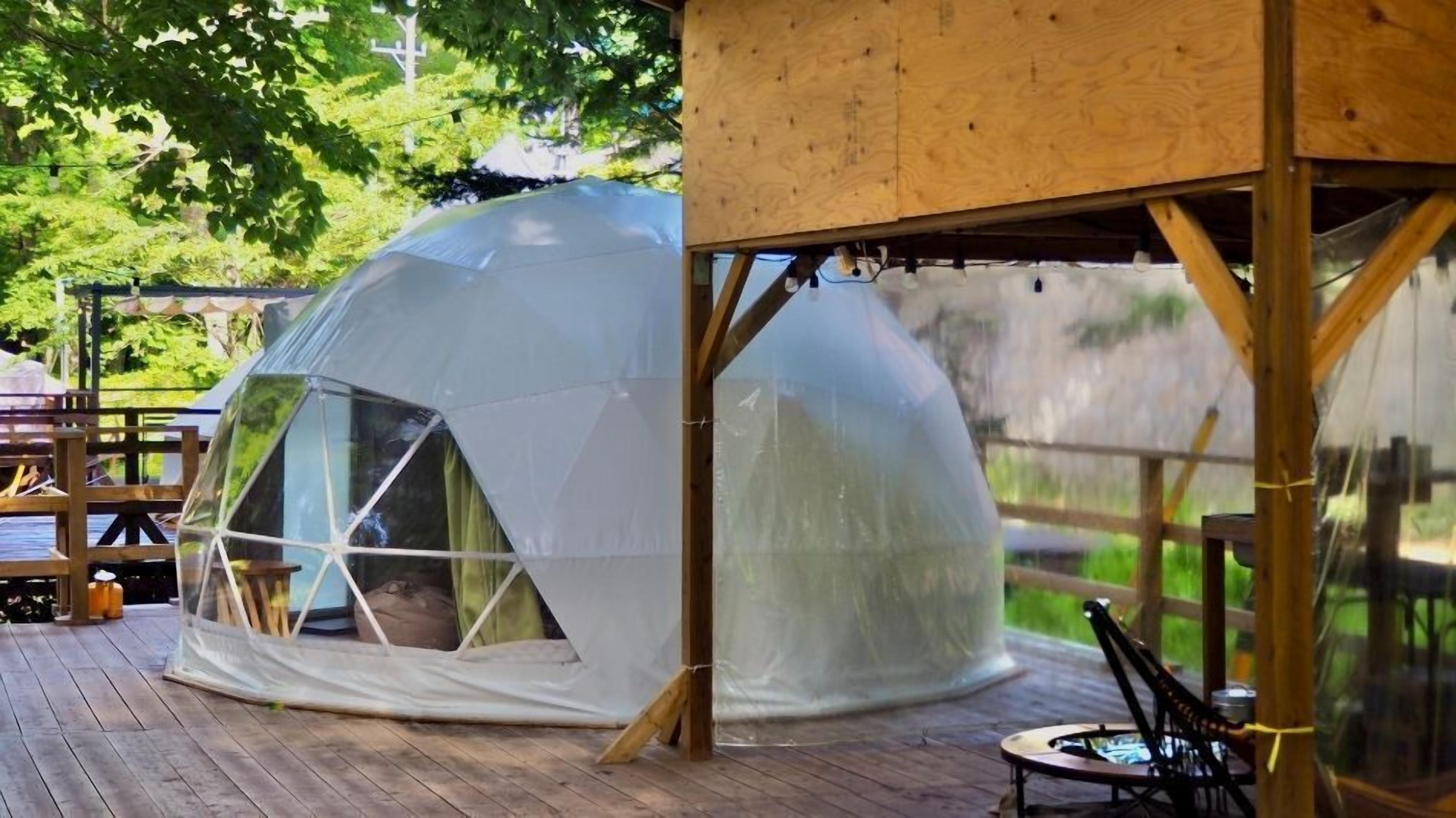 Een transparante koepeltent op een houten terras met een tafel en stoelen in de buurt.