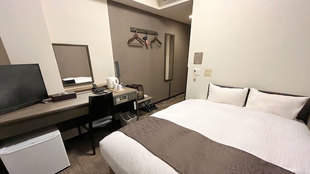 A hotel room with a bed, a desk with a computer, a small refrigerator, a mirror, and a coat rack. - Hana Hotel Isesaki (Isesaki)