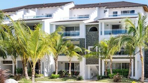 Resort com piscina, palmeiras e um prédio grande com várias varandas.