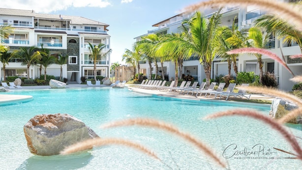 Piscina de resort com espreguiçadeiras e palmeiras, cercada por edifícios altos com varandas.