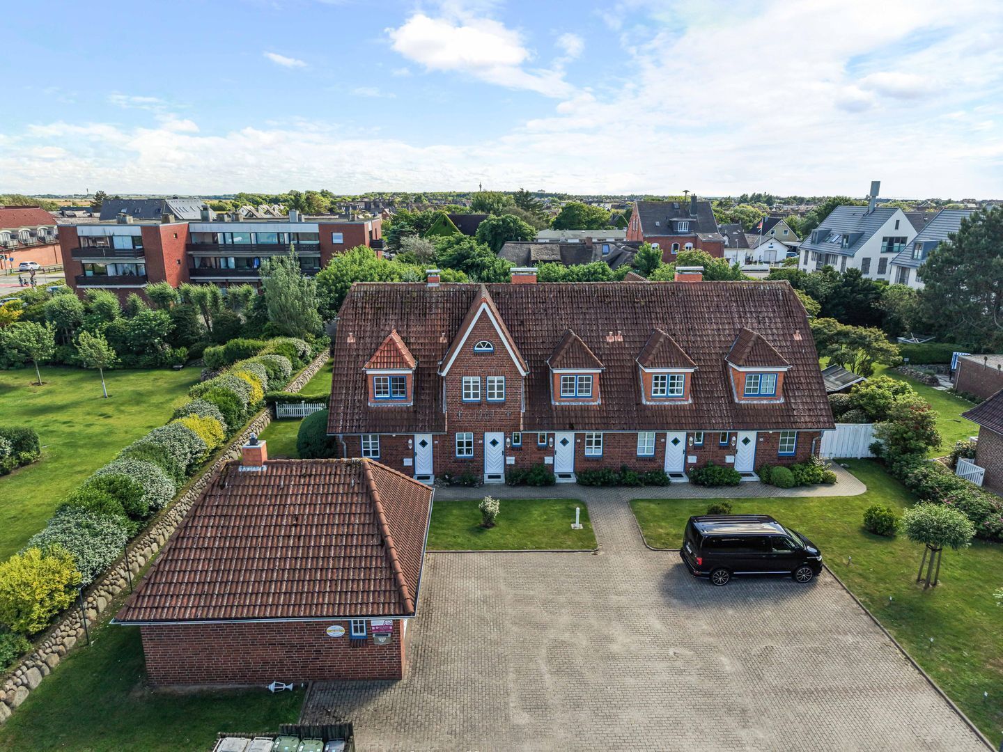A large brick house with a tiled roof, a driveway, and a parked car.