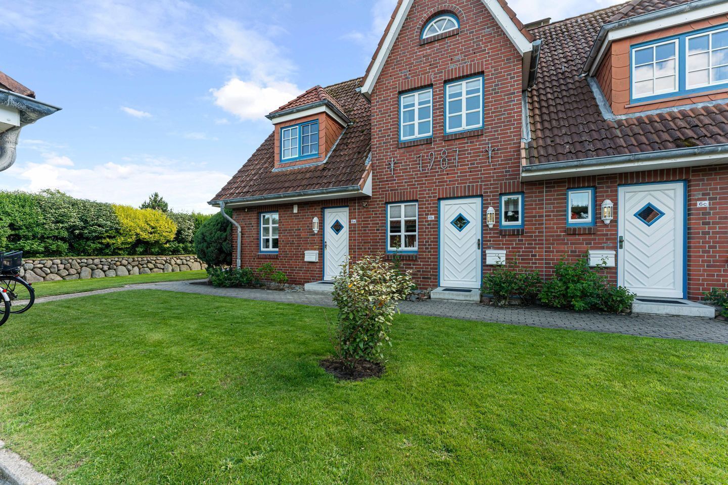 Een twee verdiepingen tellend bakstenen huis met een verzorgd gazon, een stenen muur en een kleine tuin.