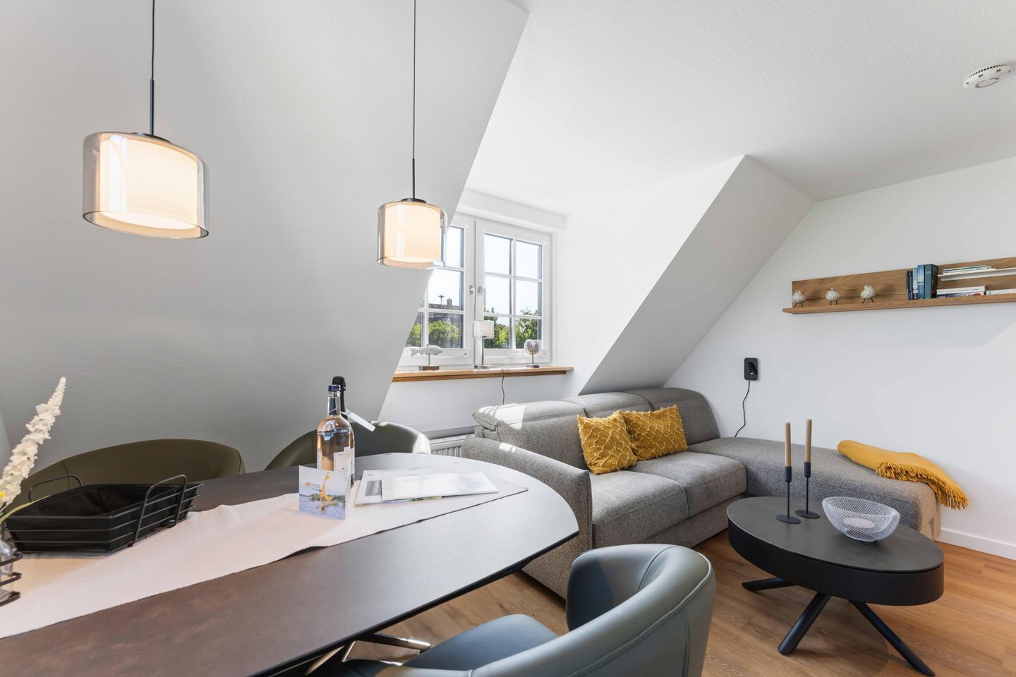 A modern loft bedroom with a dining area, a gray sofa, and a wooden shelf.