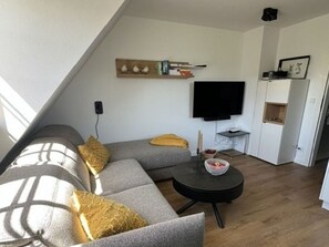 Moderni olohuone, jossa on harmaa sohva, musta sohvapöytä ja litteänäyttöinen televisio.