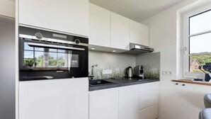 Cozinha moderna com armários brancos, um forno Siemens, uma cafeteira e uma janela com vista para o verde.