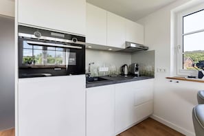 Eine moderne Küche mit weißen Schränken, einem Siemens-Ofen, einer Kaffeemaschine und einem Fenster mit Blick auf Grünflächen.