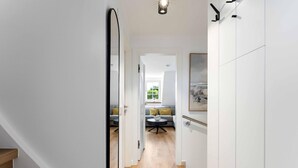 Um corredor que dá para uma sala de estar com sofá, mesa e um quadro na parede.